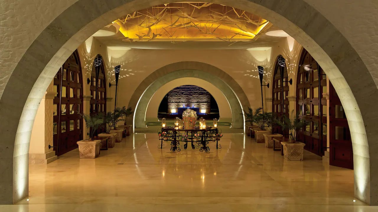 Grand hotel lobby with stone arches, marble floors, and ornate candlelit centerpiece table